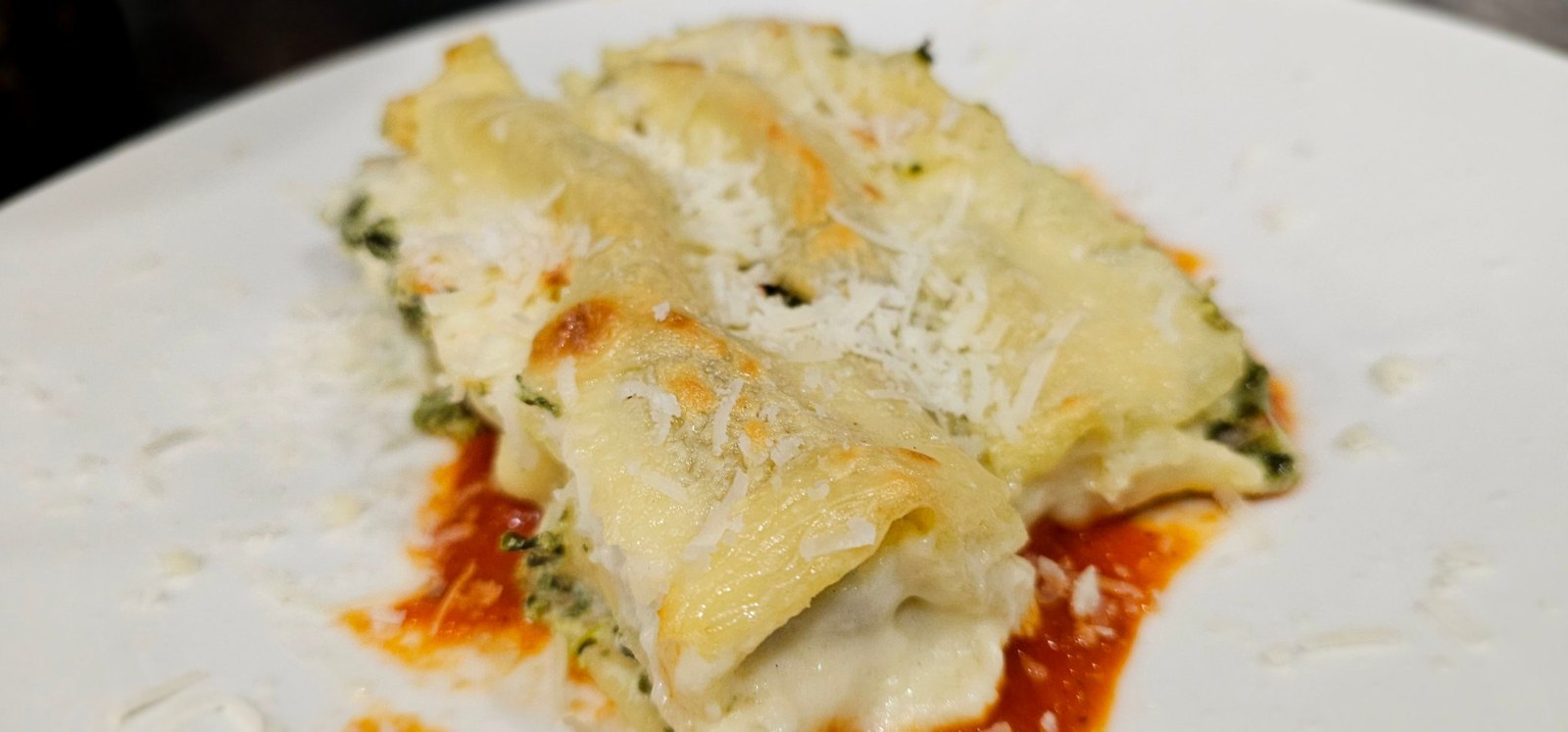 Canneloni gratinati con ripieno di verdure verdi e formaggio grattugiato, su un letto di salsa di pomodoro