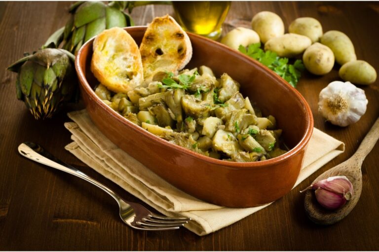 Carciofi in umido con patate in una terrina di terracotta, con crostini di pane, aglio e patate
