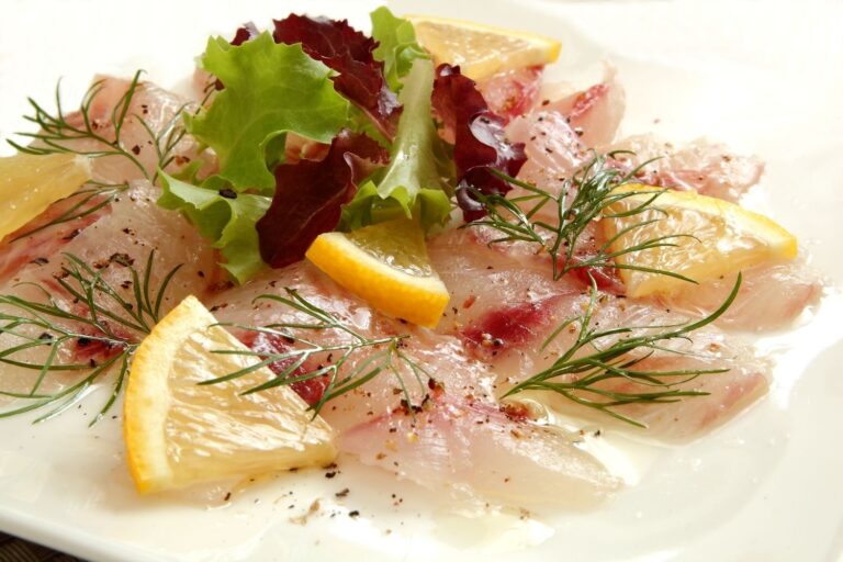 Carpaccio di pesce con misticanza, aneto e fette di limone su piatto bianco