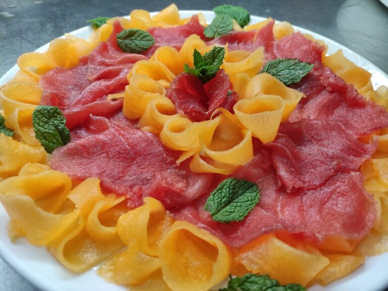 Carpaccio di tonno rosso con nastri di melone retato e foglie di menta, su piatto bianco