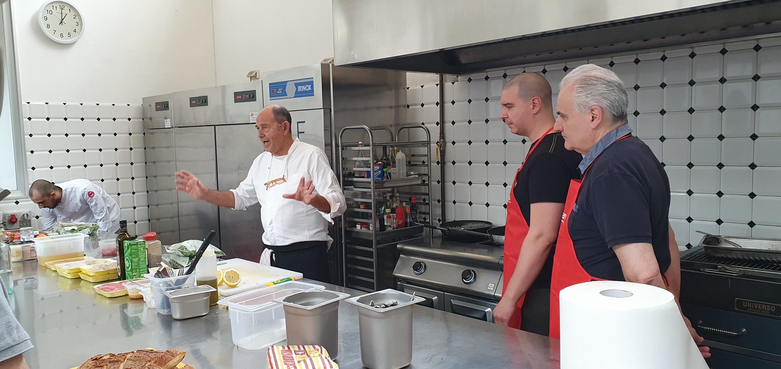 Salvo Nicastro, chef, mostra la preparazione ai partecipanti con il grembiule rosso durante una lezione di cucina per Conad