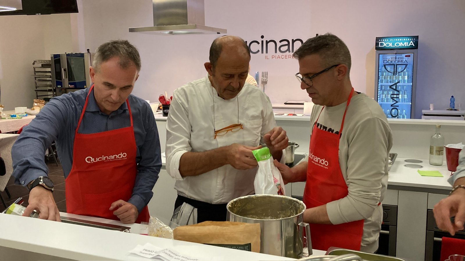 Salvo Nicastro, chef, mostra un ingrediente a due allievi durante una lezione di cucina a Qucinando