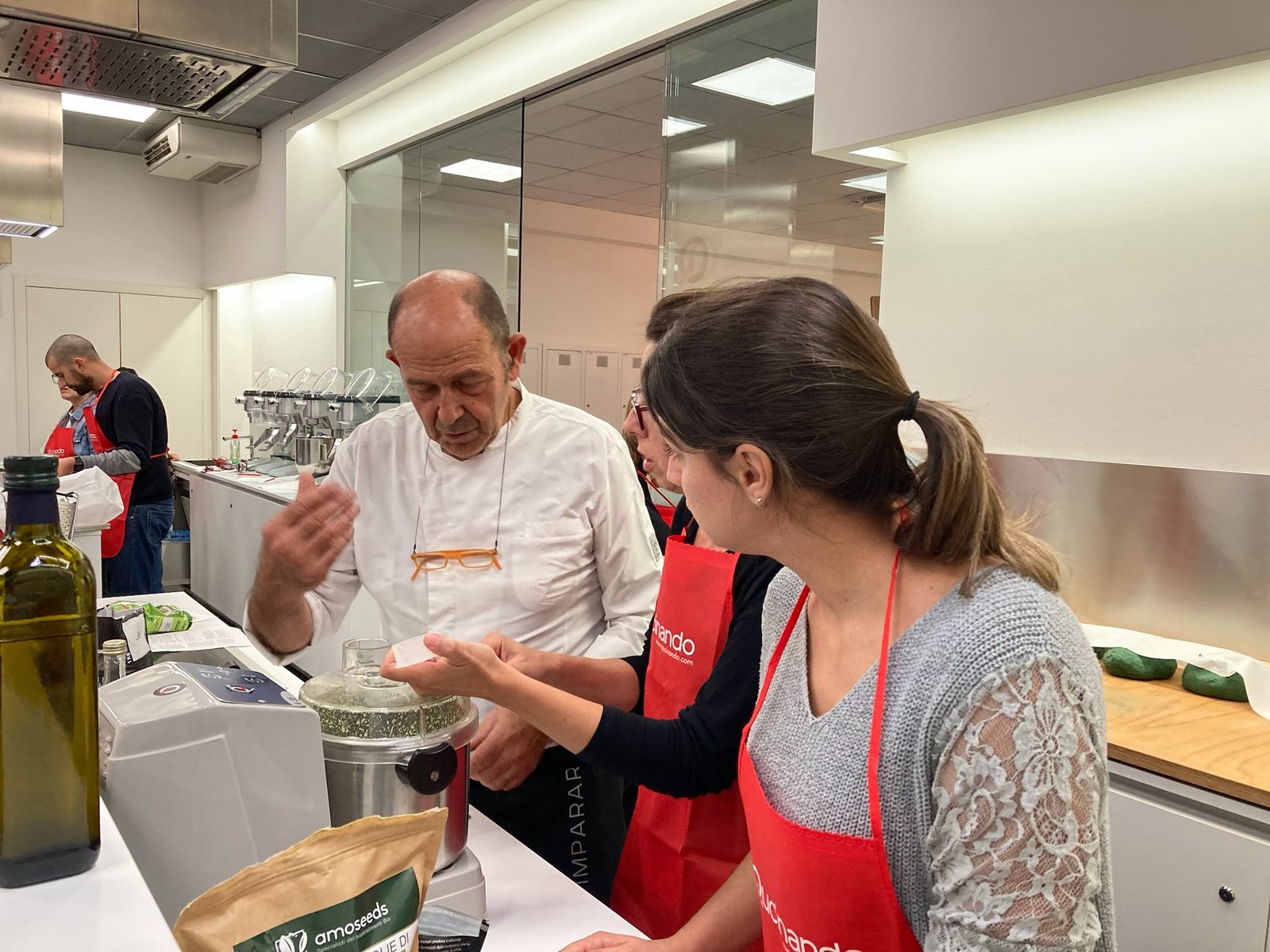 Salvo Nicastro, chef, mostra un ingrediente a due allieve durante una lezione di cucina a Qucinando