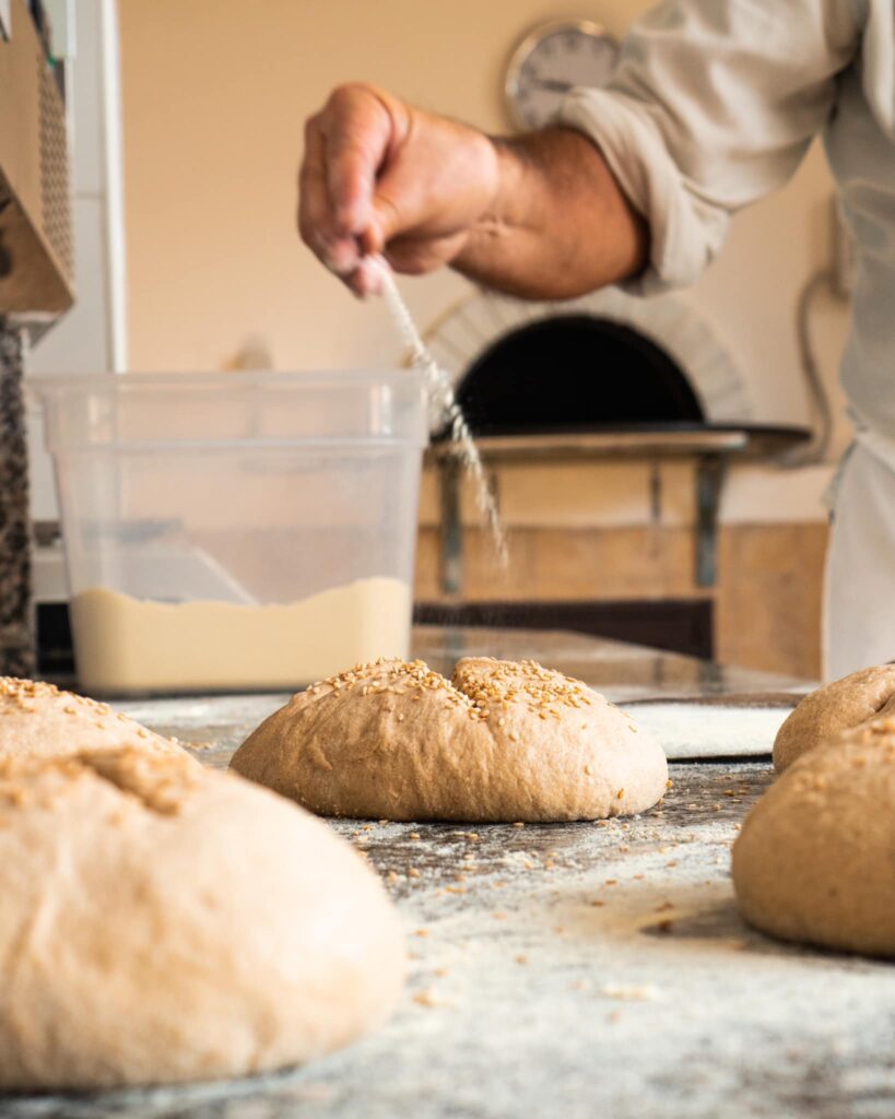 Pagnotte di pane a lievito madre pronte per il forno sul piano di lavoro, con farina e semi