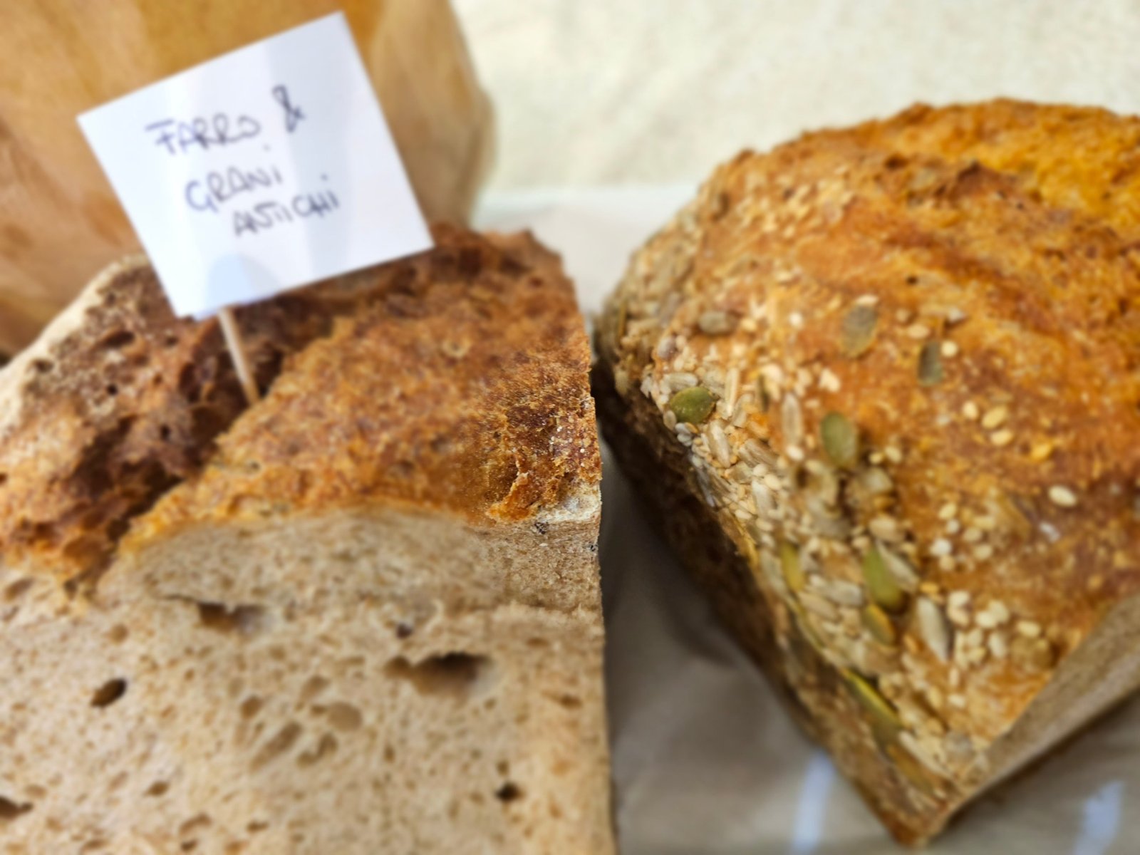 Pane di farro e grani antichi, con il cartellino scritto a mano, accanto a un pane ai semi