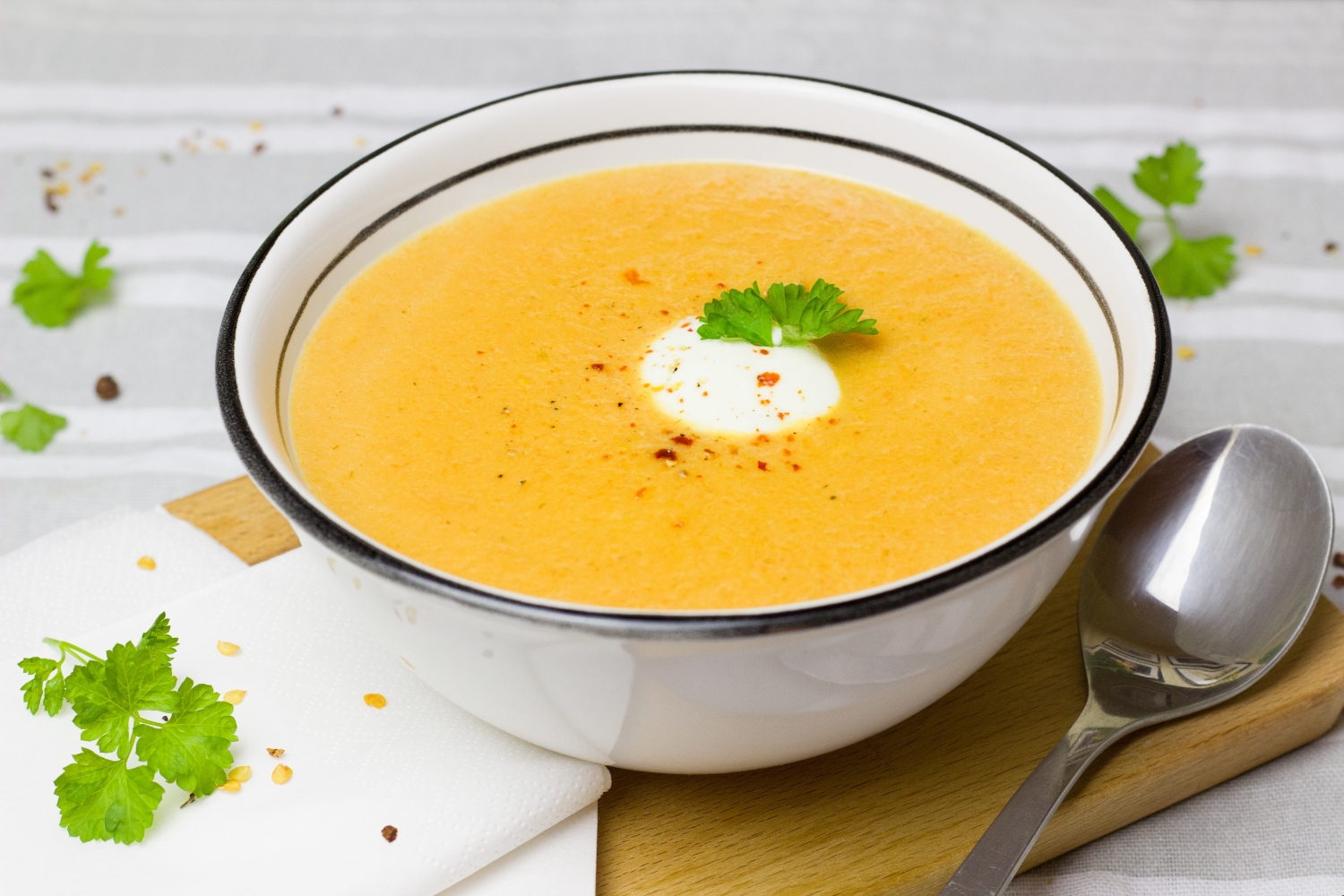 Passato di carote e zenzero in ciotola bianca con un ciuffo di yogurt e prezzemolo