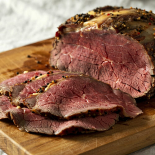 Roast beef con crosta di pepe e senape in grani, affettato su un tagliere di legno