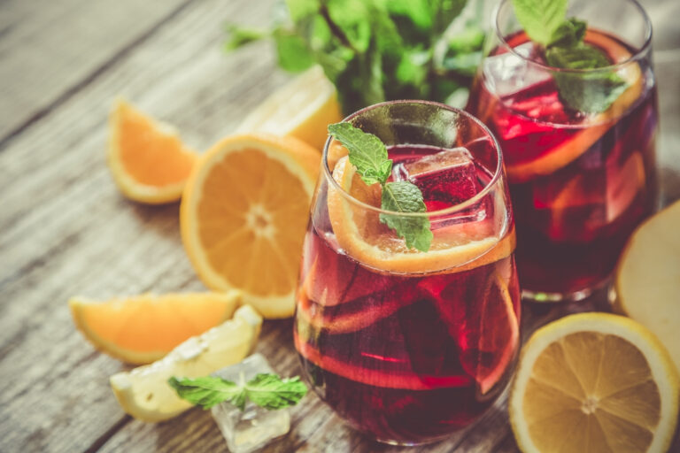 Sangria in due bicchieri con ghiaccio e foglie di menta, circondata da fette di arancia e di limone su un tavolo di legno
