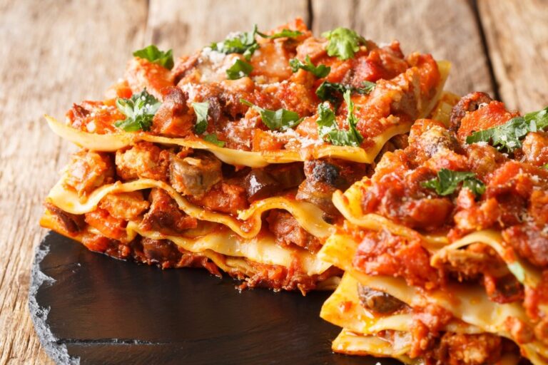 Vincisgrassi marchigiani: pasta al forno a strati con ragù di carni e prezzemolo, serviti su un piatto di ardesia